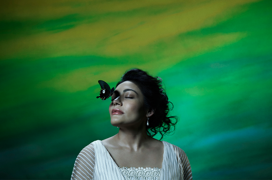 woman in white standing with butterfly on face in front of green background