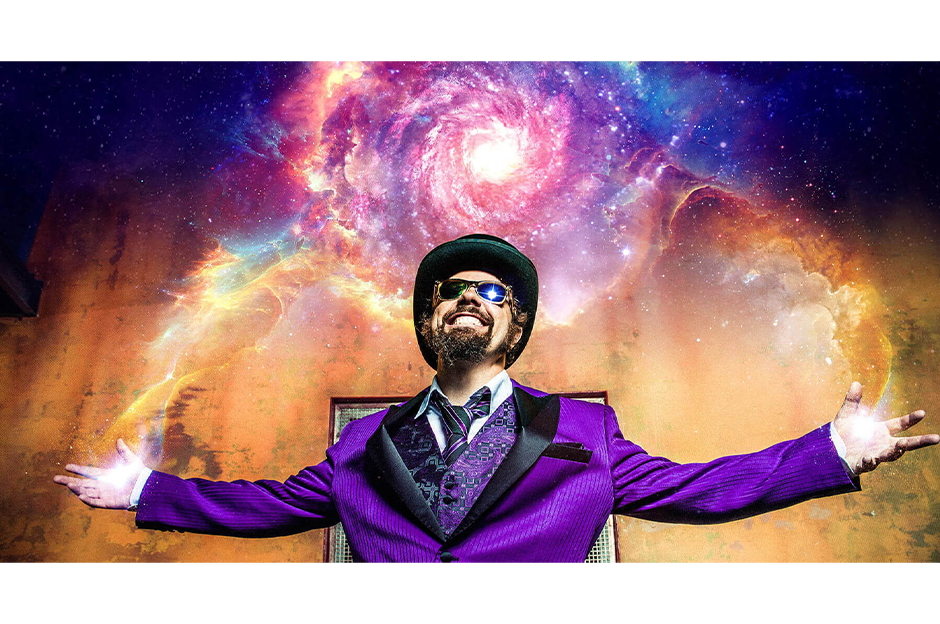 bearded man with top hat in purple suit with arms stretched out with galaxy background