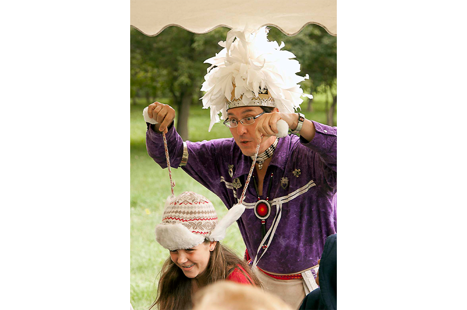 man dressed in native american clothing playing with kids hat 
