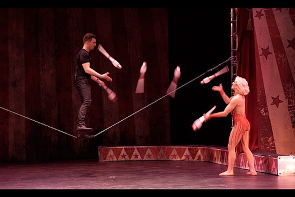 man balancing on rope juggling with woman from the ground